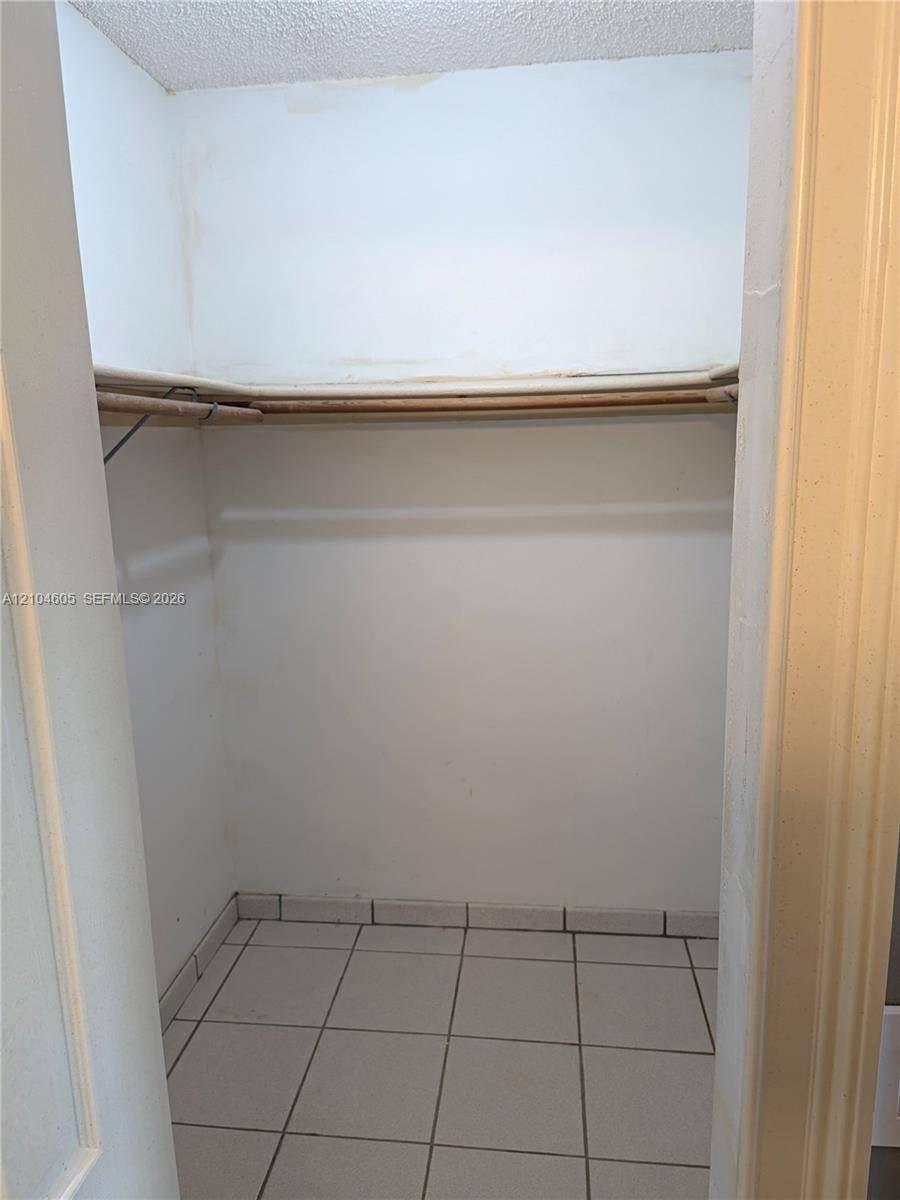 Storage closet featuring tile flooring, a built-in overhead shelf, and a support rod