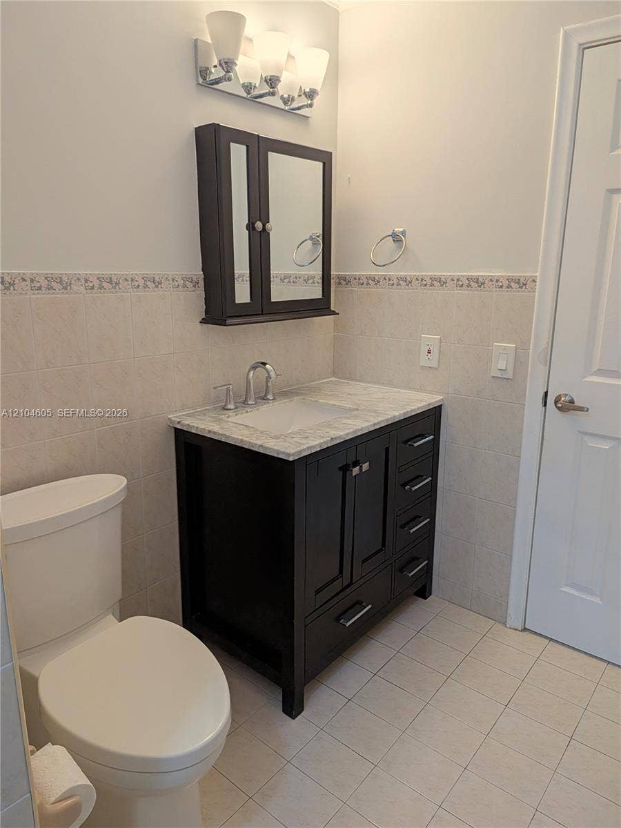 Dark-finish vanity featuring stone-style countertop with integrated sink, matching wall-mounted medicine cabinet, three-light fixture with glass shades, and ceramic tile wainscoting