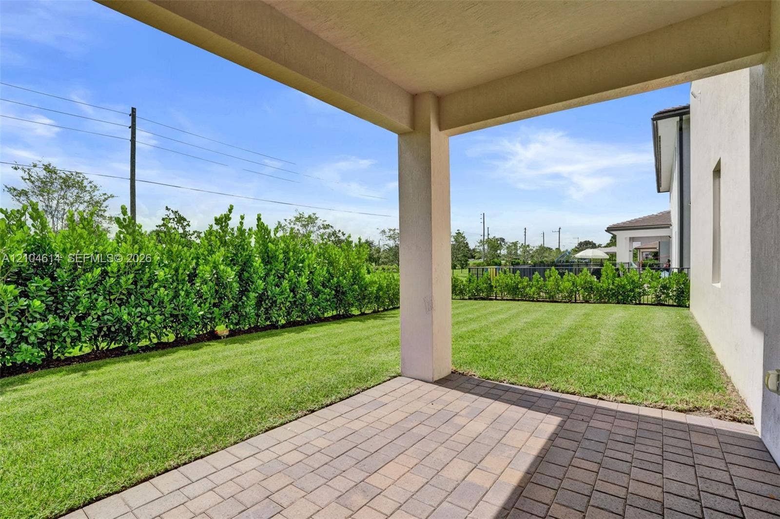12240 SW 44th Court, Davie, FL 33330 Covered patio featuring paver flooring, leading to a manicured lawn and mature privacy hedges