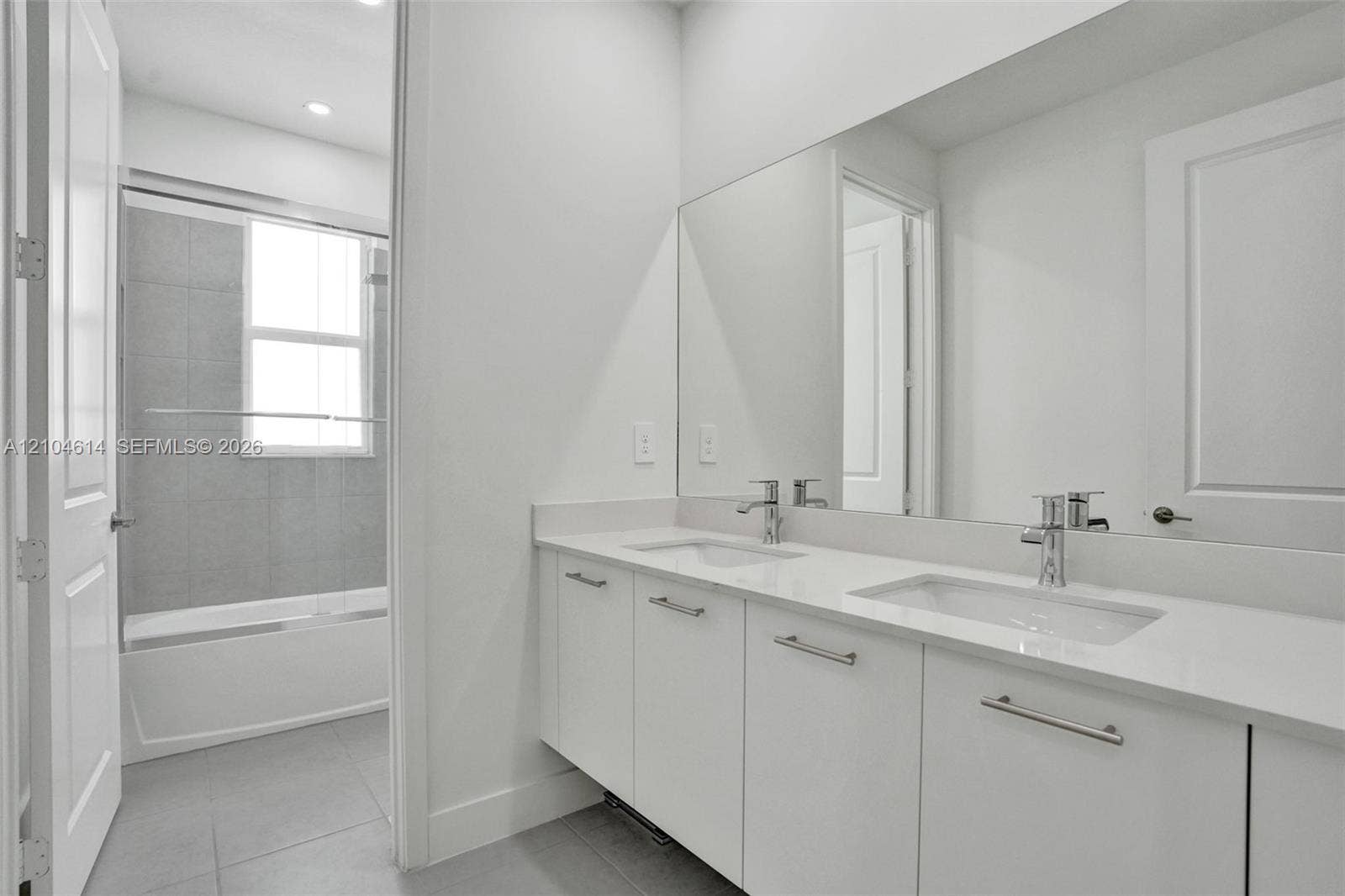 12240 SW 44th Court, Davie, FL 33330 Dual vanity with chrome fixtures and ample counter space, full-width mirror, recessed lighting, and a bathtub with a sliding glass enclosure