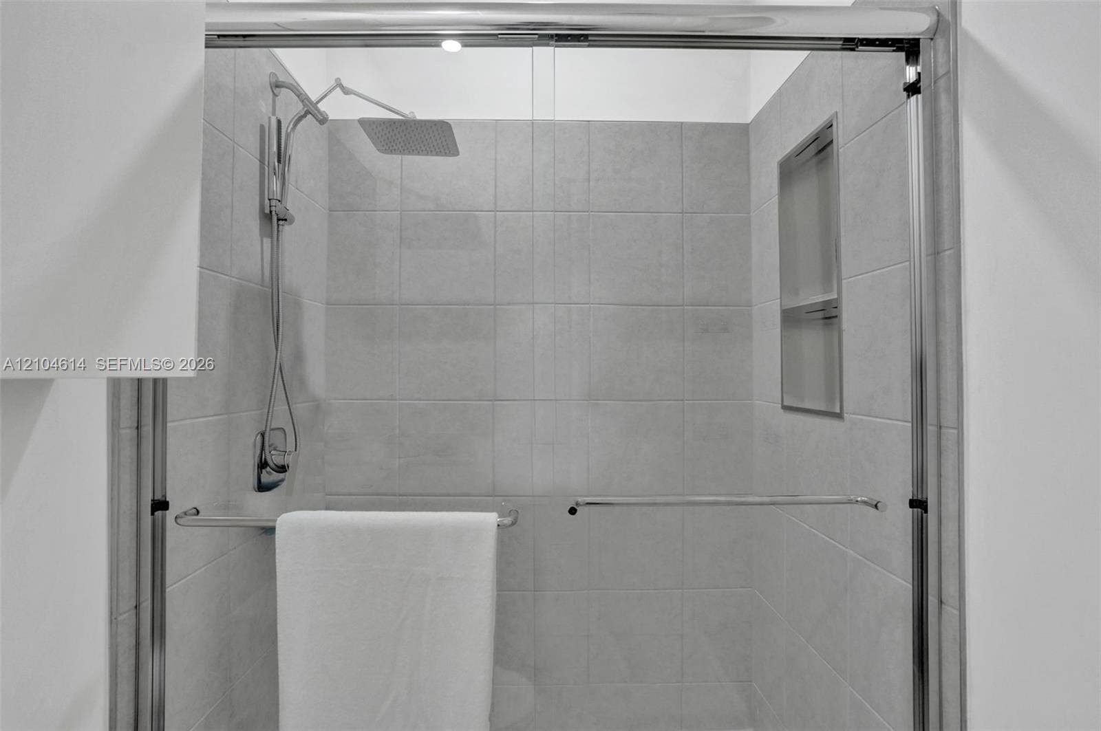 12240 SW 44th Court, Davie, FL 33330 Frameless glass shower enclosure featuring a rectangular rain showerhead and a built-in shower niche