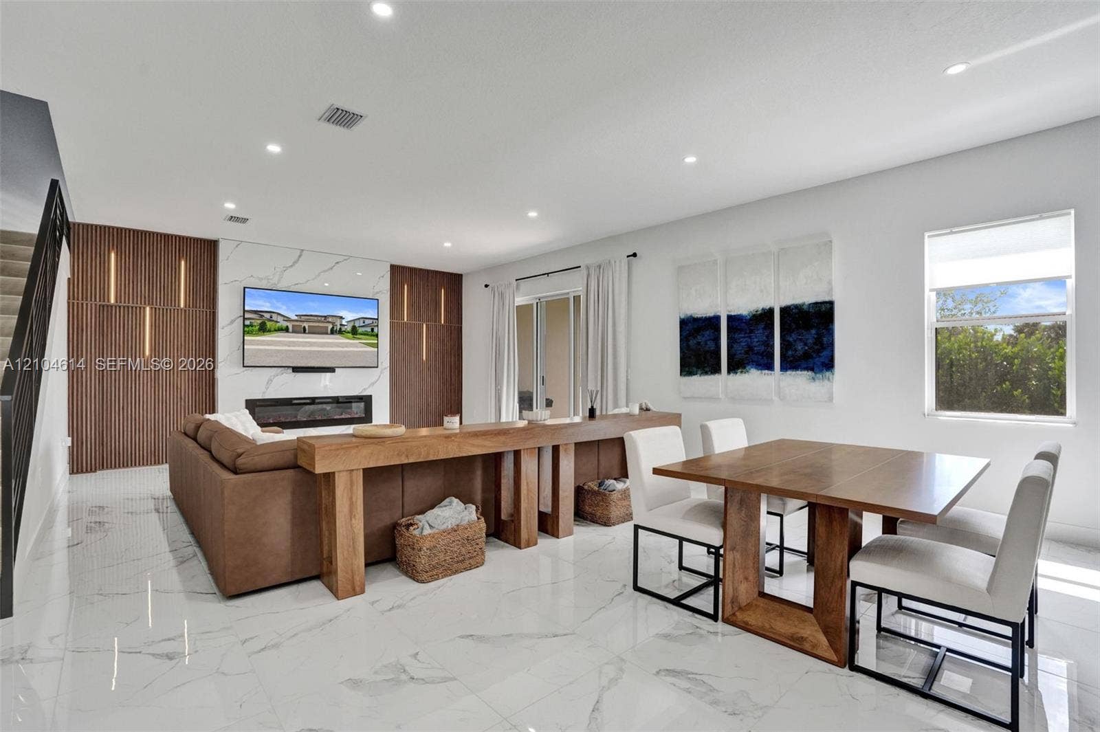 12240 SW 44th Court, Davie, FL 33330 Open-concept living area featuring large format marble-look tile flooring, a built-in electric fireplace, and a wood-slat accent wall with integrated lighting
