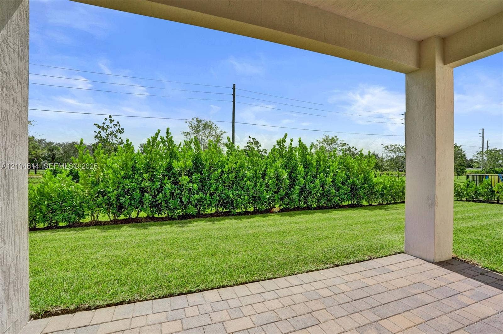 12240 SW 44th Court, Davie, FL 33330 Expansive outdoor living area featuring a covered patio with paver flooring, lush lawn, and mature privacy hedging