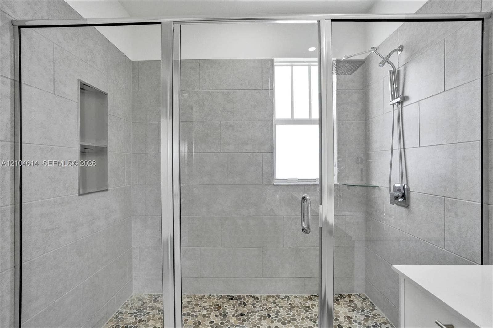 12240 SW 44th Court, Davie, FL 33330 Shower with sliding glass enclosure, light gray tile walls, built-in recessed shelf, and pebble-finish flooring