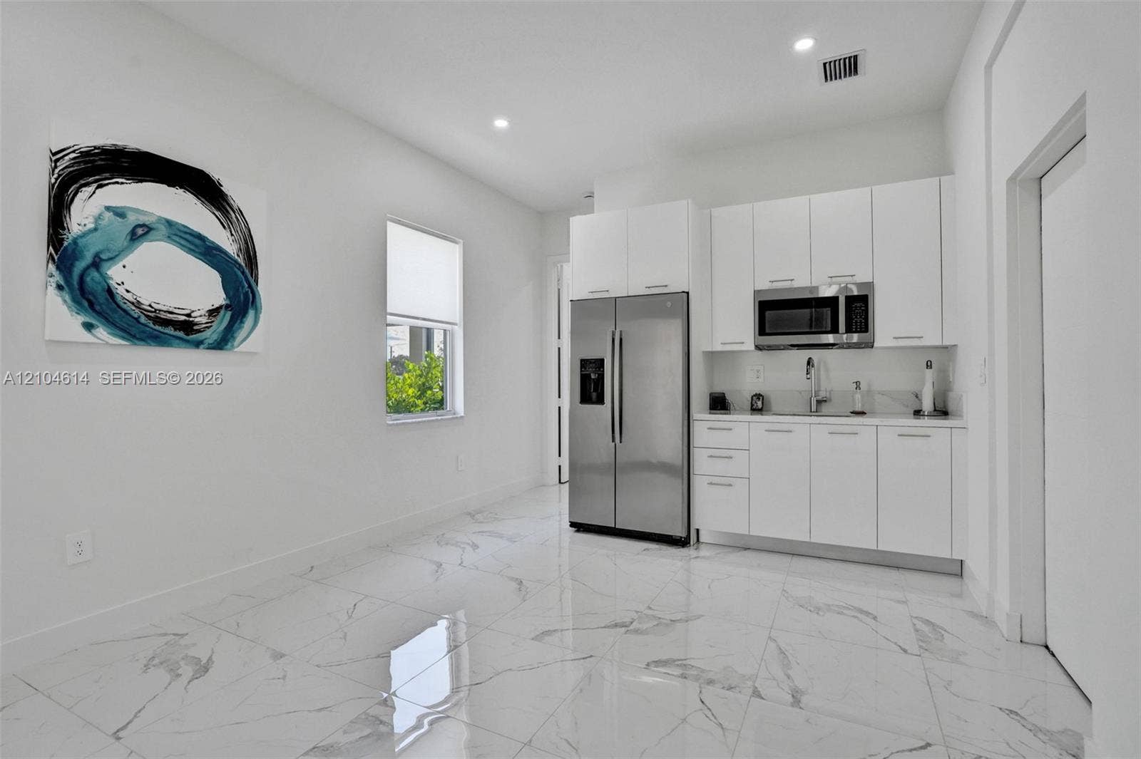 12240 SW 44th Court, Davie, FL 33330 White shaker-style cabinetry with stainless steel hardware, stainless steel side-by-side refrigerator, stainless steel microwave, and polished tile flooring