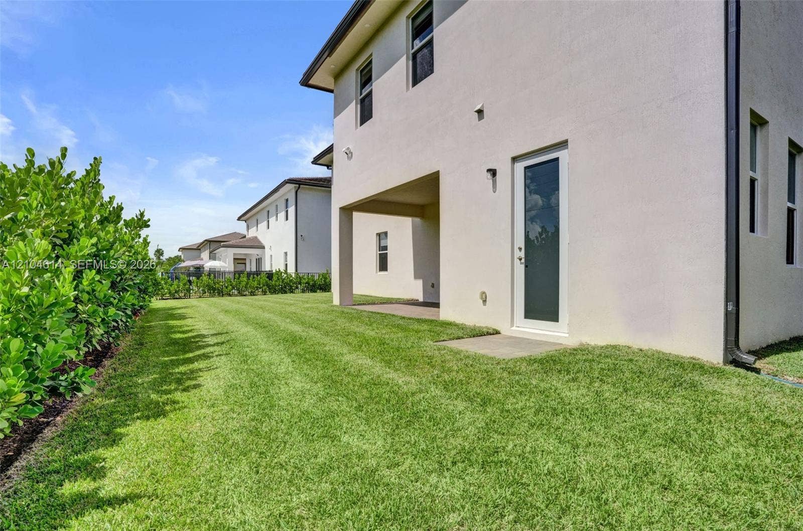 12240 SW 44th Court, Davie, FL 33330 Expansive exterior with light-toned stucco, multiple windows, covered patio, and a privacy hedge