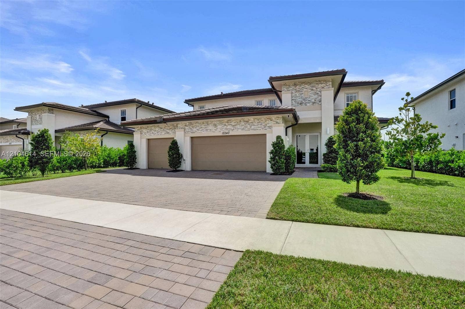 12240 SW 44th Court, Davie, FL 33330 Contemporary stucco exterior with stone accents, featuring a two-car garage, a paver driveway, and a manicured lawn