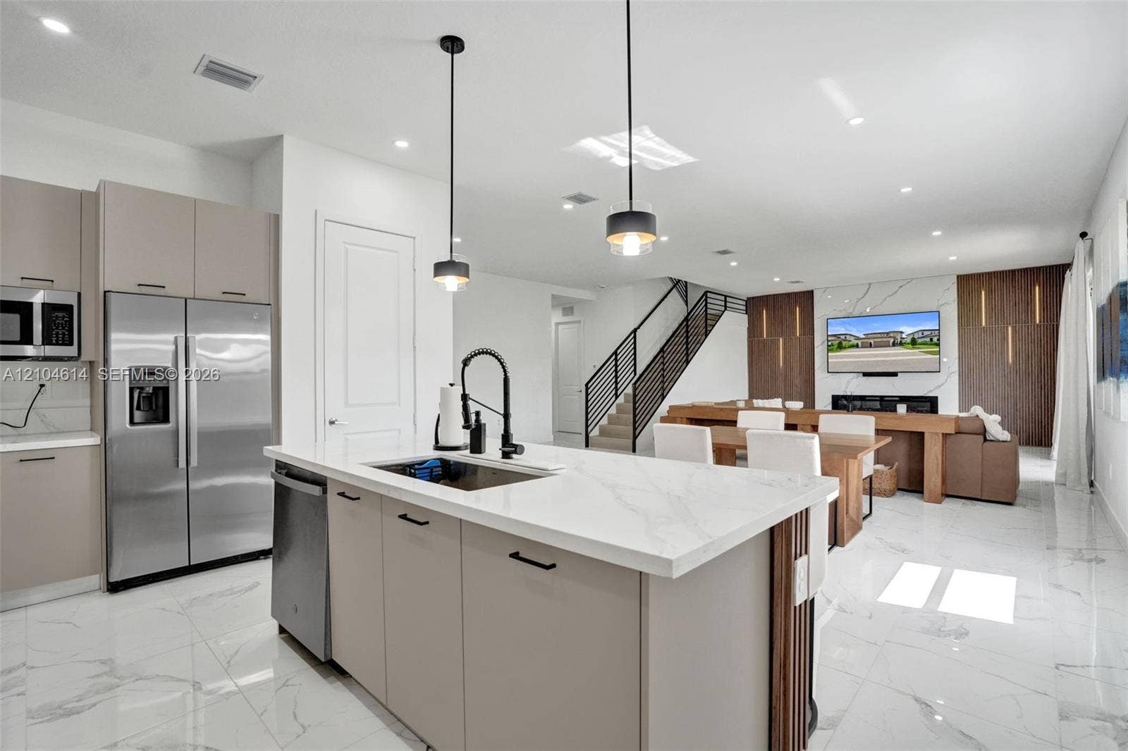 12240 SW 44th Court, Davie, FL 33330 Open-concept living space with large format tile flooring, a kitchen island with stone countertop, stainless steel appliances, a modern staircase with metal railings, and a feature wall with integrated lighting