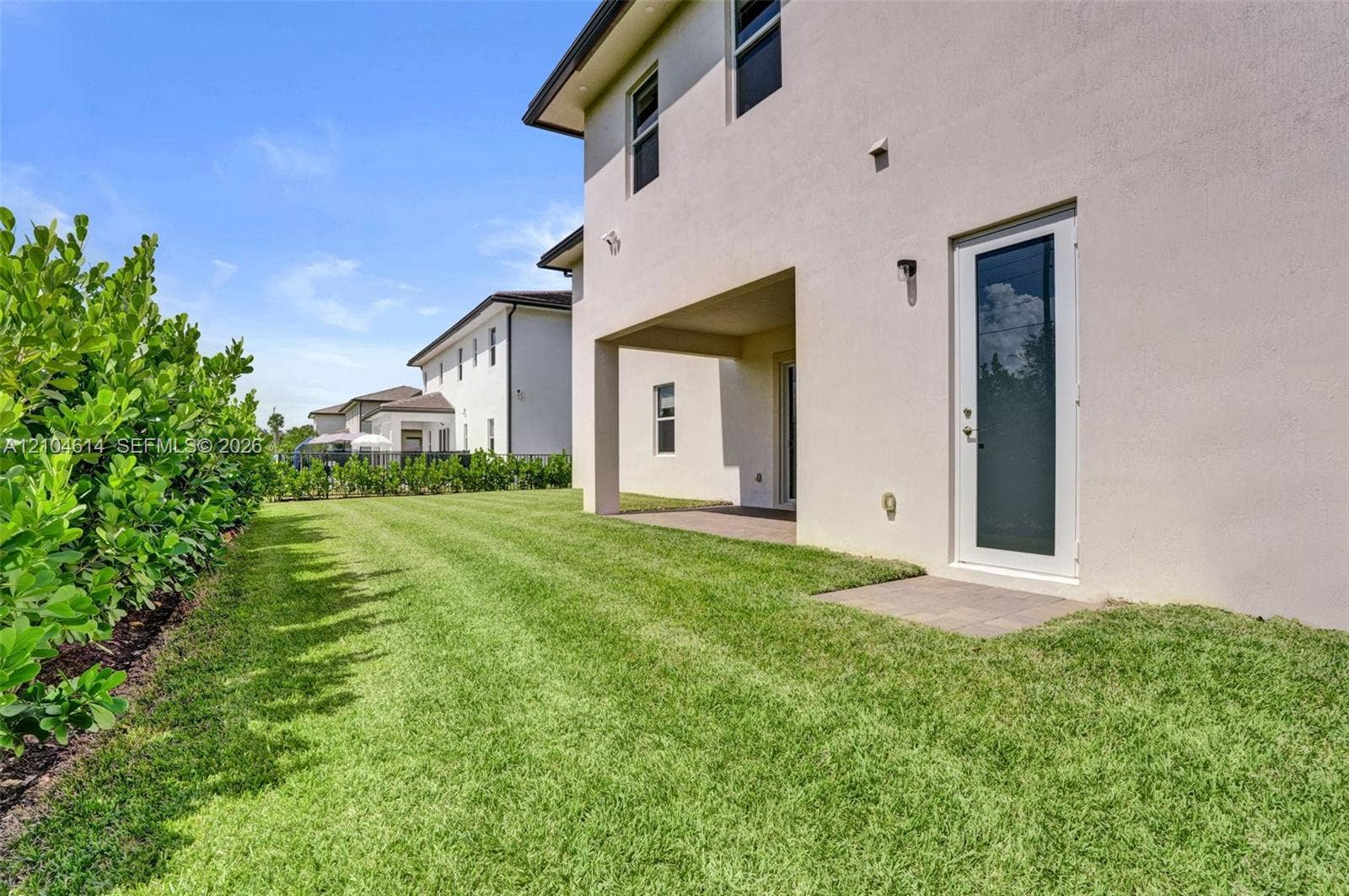 12240 SW 44th Court, Davie, FL 33330 Expansive green lawn with established hedges, featuring a covered patio and a separate exterior door with a full-light panel