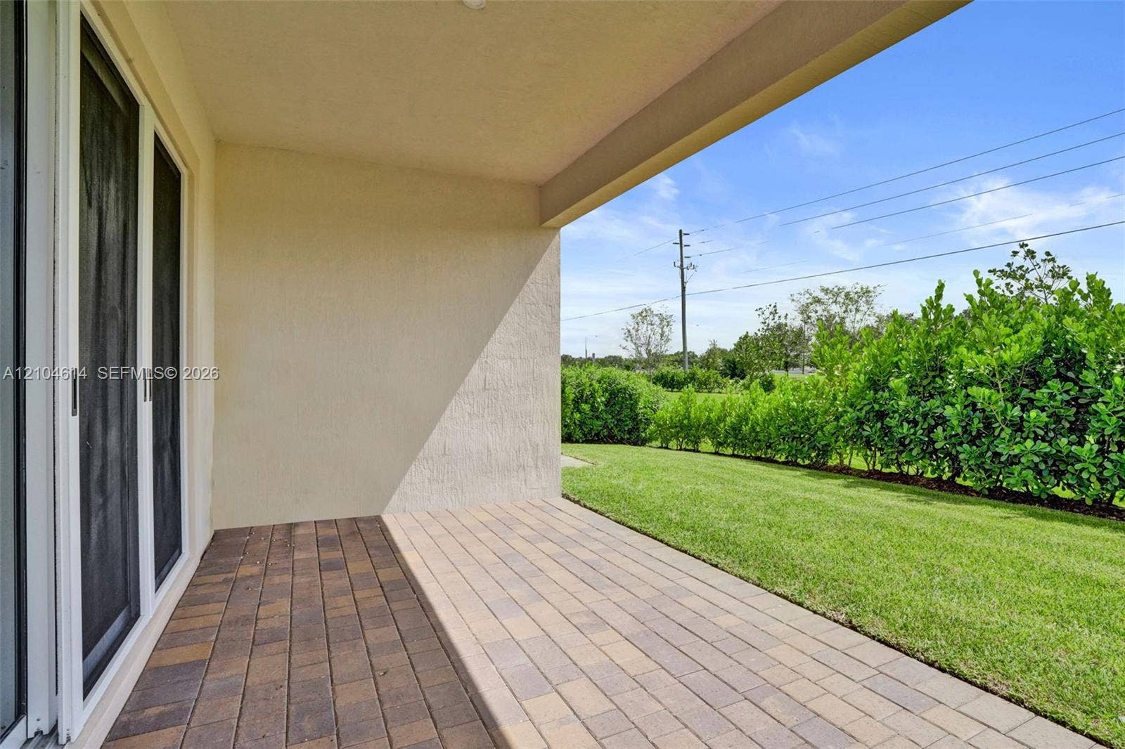 12240 SW 44th Court, Davie, FL 33330 Covered patio with paver flooring, stucco exterior, sliding glass doors, and a manicured lawn with privacy hedges