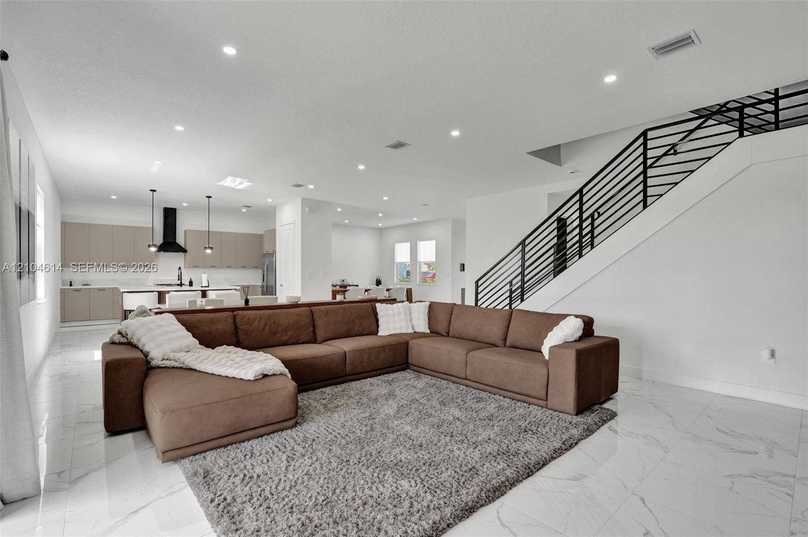 12240 SW 44th Court, Davie, FL 33330 Open-concept living space featuring high ceilings, recessed lighting, large format tile flooring, and a contemporary staircase with black metal railings