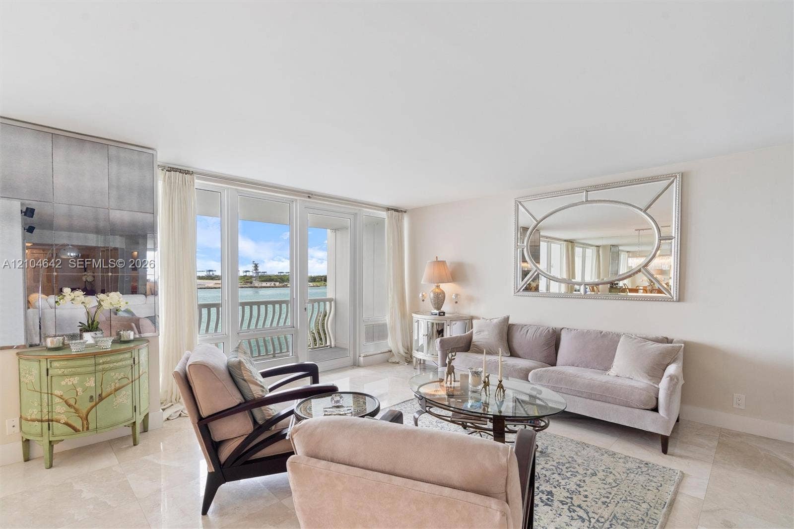 Living area featuring light-toned stone tile flooring, floor-to-ceiling glass panel windows, sliding glass door access to a balcony, and a mirrored wall accent