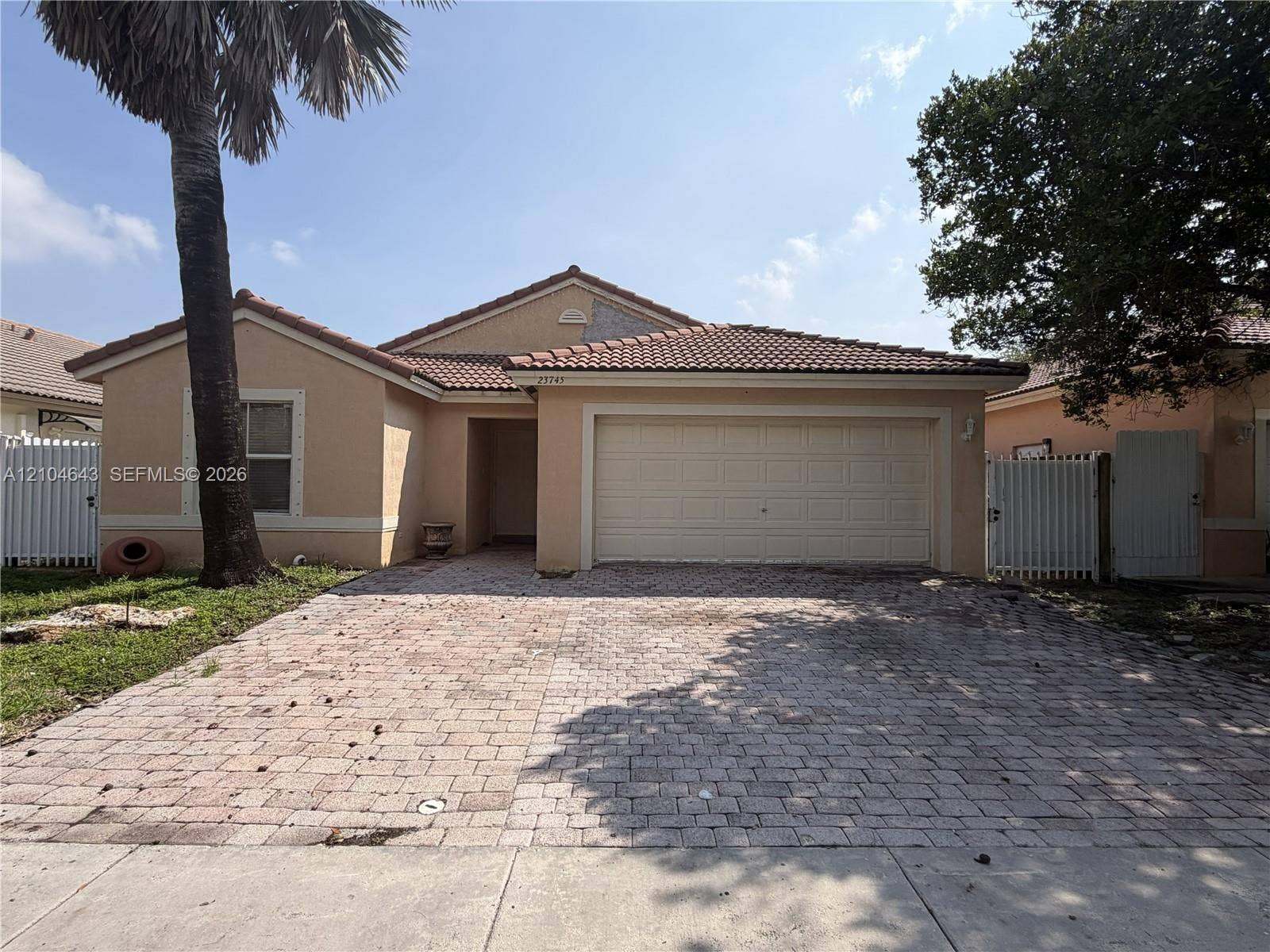 Stucco exterior with a tiled roof, paver driveway, and an attached two-car garage