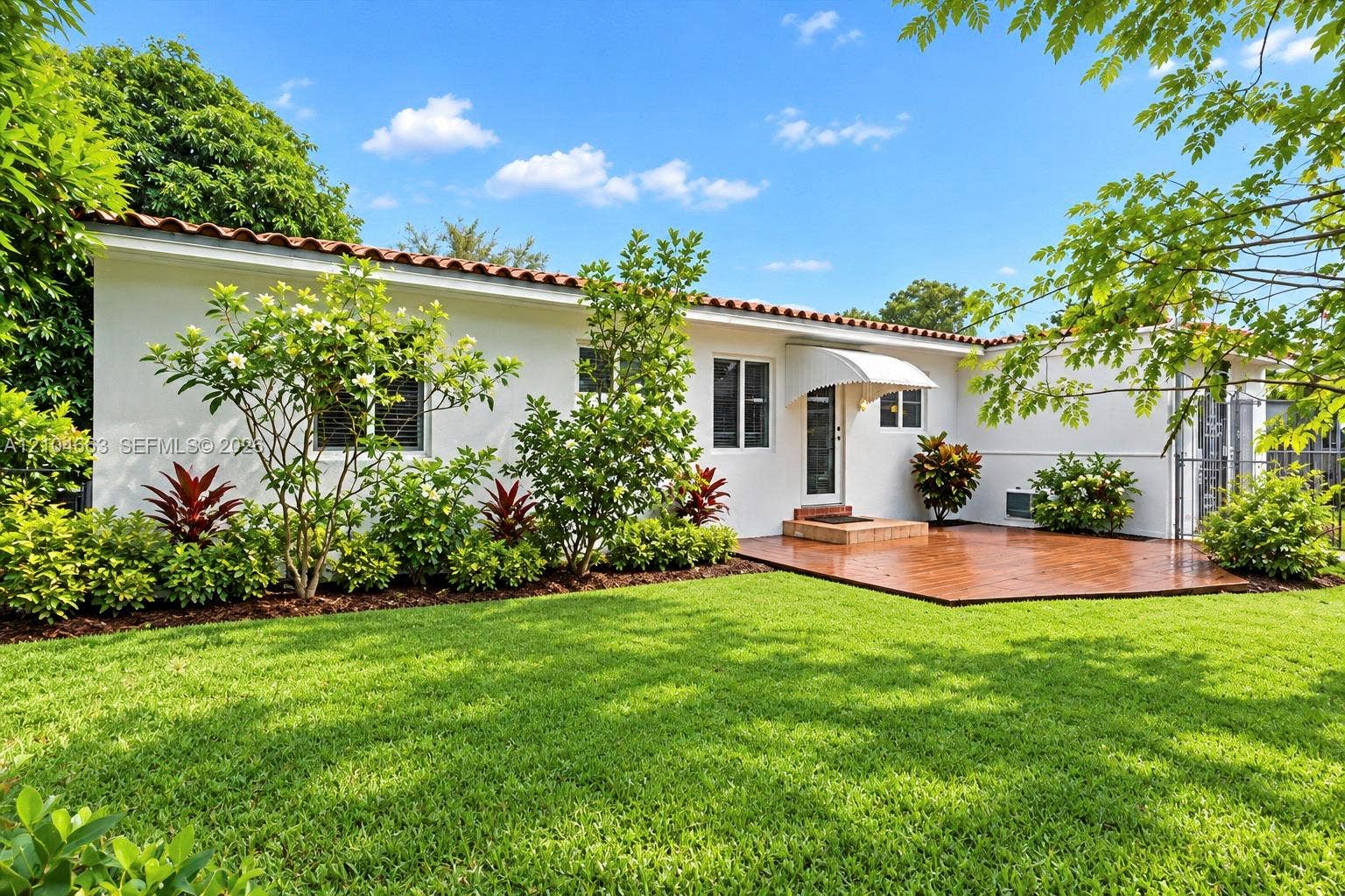 305 NW 111th Street, Miami Shores, FL 33168 Stucco exterior featuring a terracotta tile roof, manicured lawn, stamped concrete patio, and mature landscaping