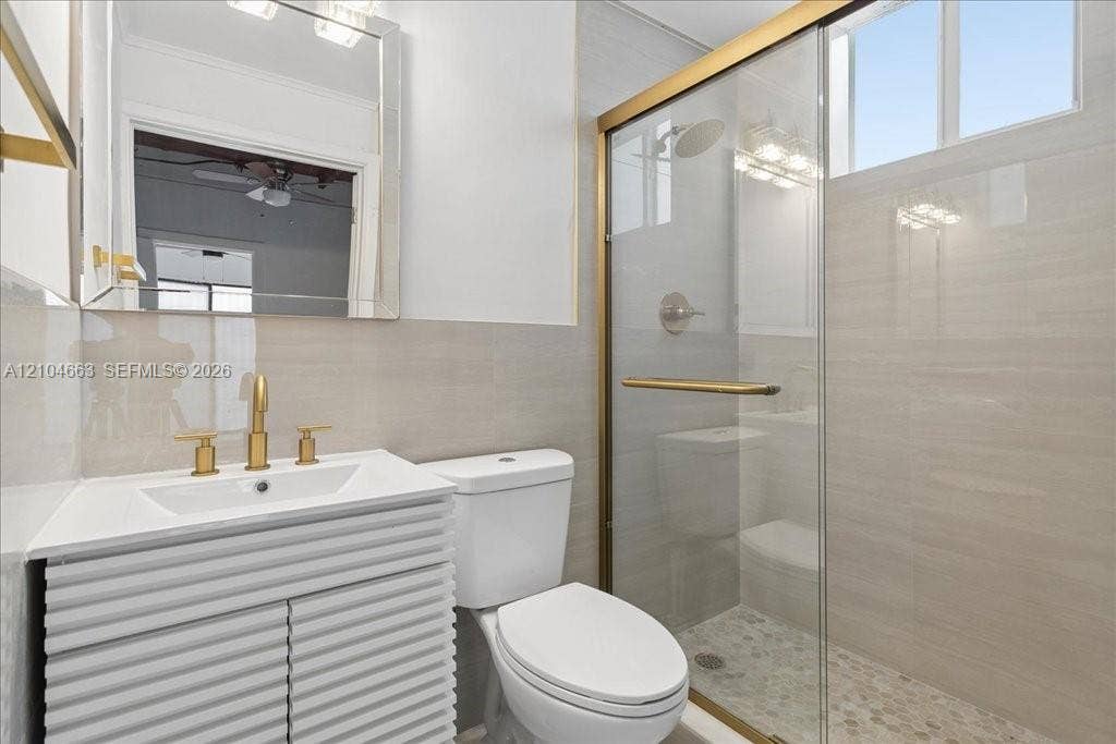 305 NW 111th Street, Miami Shores, FL 33168 Bathroom featuring a white textured vanity cabinet, gold-tone fixtures, a walk-in shower with a glass enclosure, and light-toned wall tile