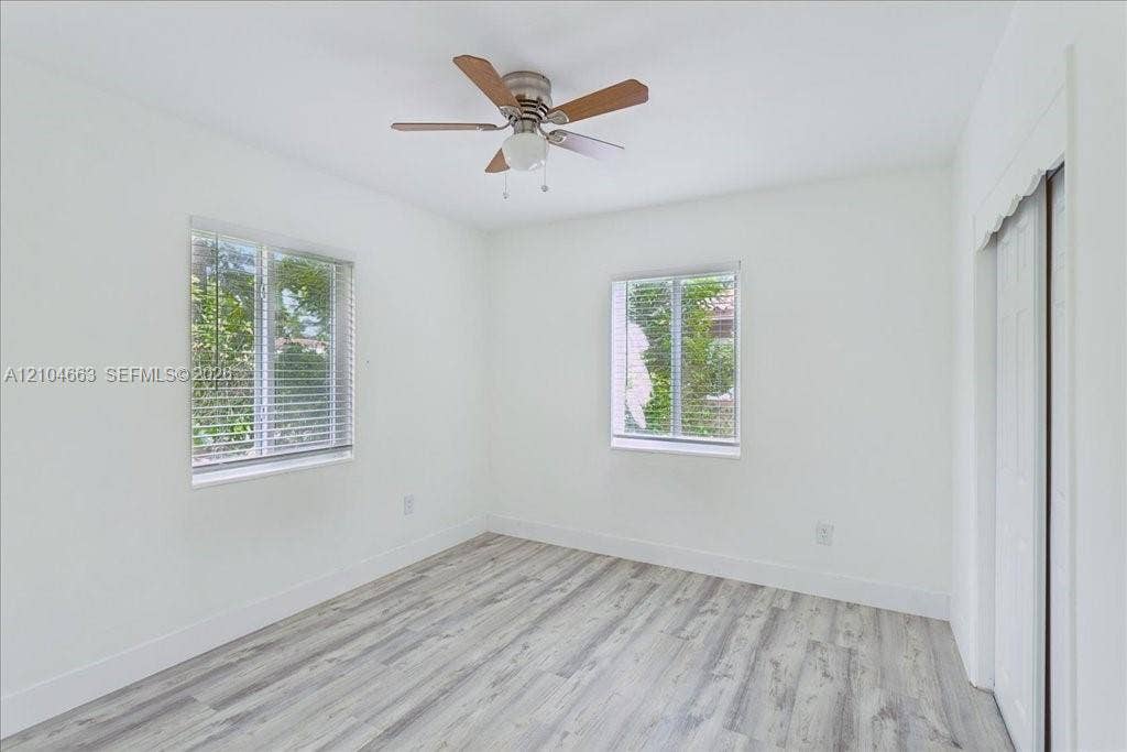 305 NW 111th Street, Miami Shores, FL 33168 Neutral-toned room featuring wood-finish flooring, two windows with horizontal blinds, a ceiling fan with light fixture, and a sliding-door closet