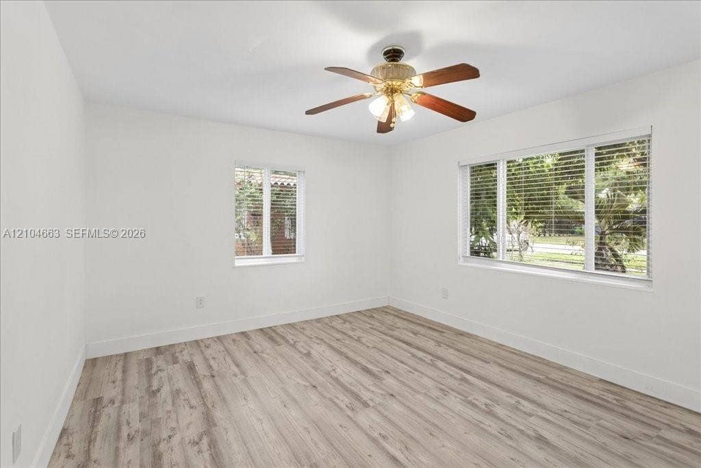 305 NW 111th Street, Miami Shores, FL 33168 Room featuring wood-finish flooring, white walls, two multi-pane windows with horizontal blinds, and a central ceiling fan with integrated lighting