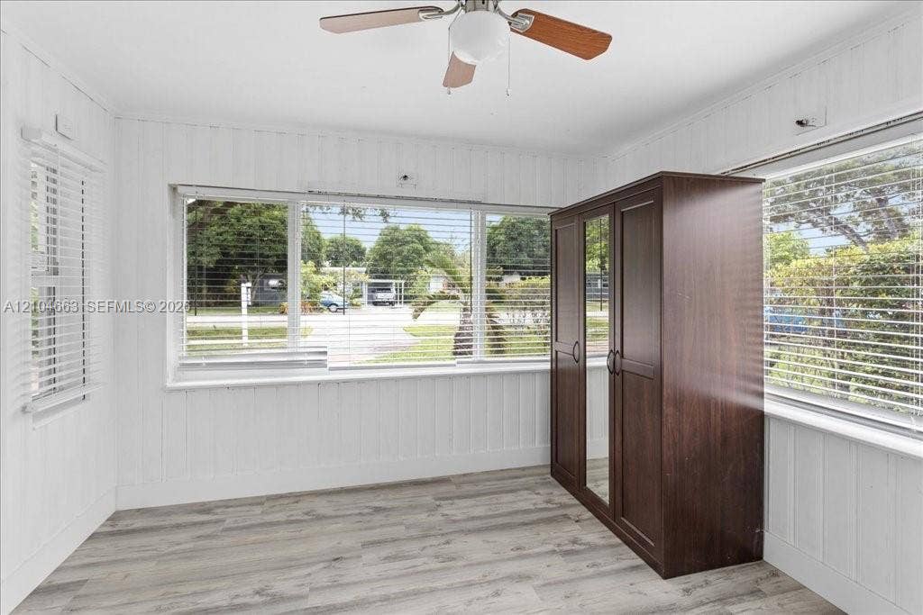 305 NW 111th Street, Miami Shores, FL 33168 Room featuring wood-finish flooring, vertical plank wall paneling, large windows with horizontal blinds, and a ceiling fan with integrated lighting