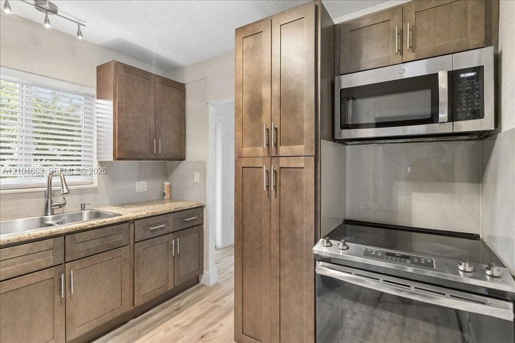 305 NW 111th Street, Miami Shores, FL 33168 Kitchen featuring wood-finish cabinetry, stone-surface countertops, stainless steel appliances, and integrated track lighting