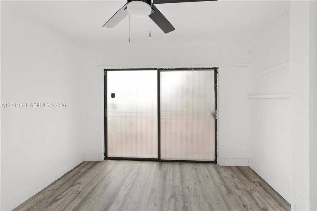 305 NW 111th Street, Miami Shores, FL 33168 Room featuring wood-finish flooring, sliding glass door, and a ceiling-mounted light fixture with a fan
