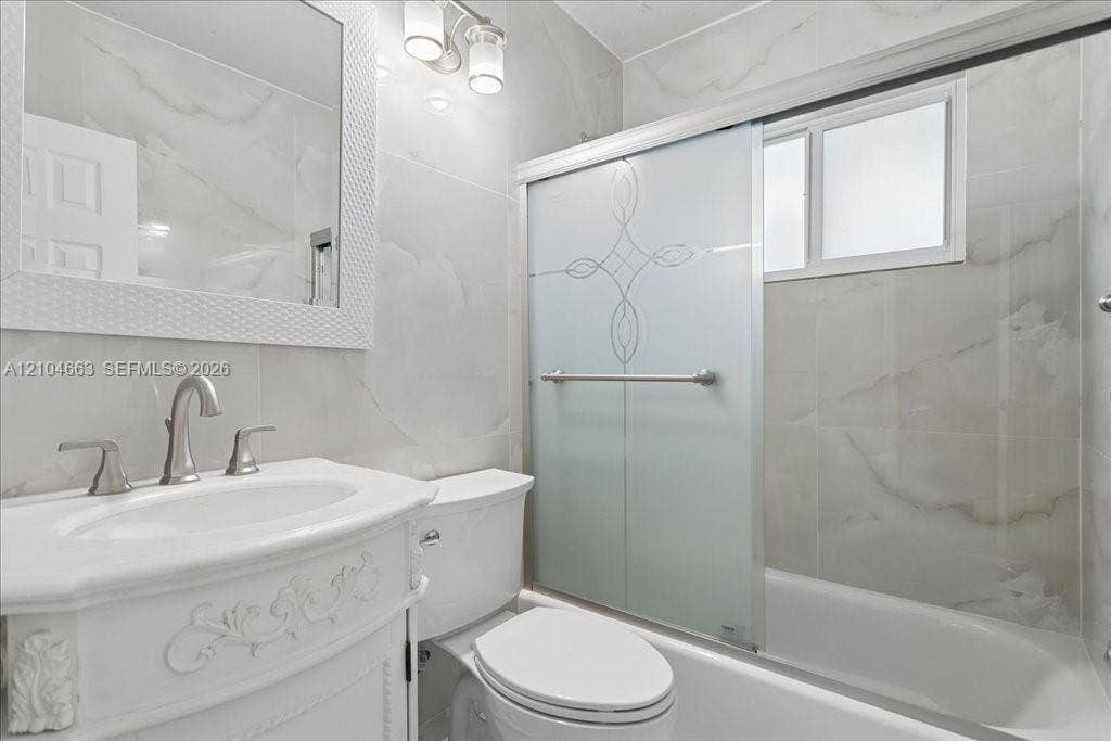 305 NW 111th Street, Miami Shores, FL 33168 Bathroom featuring vanity with ornate detailing, wall-mounted mirror, sliding shower door with decorative etching, and large-format tile surround