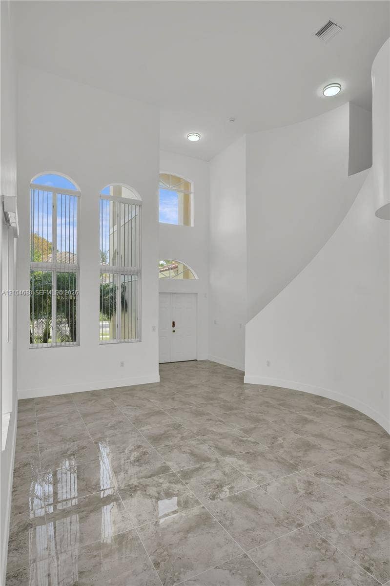High-ceilinged entry featuring stone-finish tile flooring, arched windows, recessed lighting, and a curved architectural wall