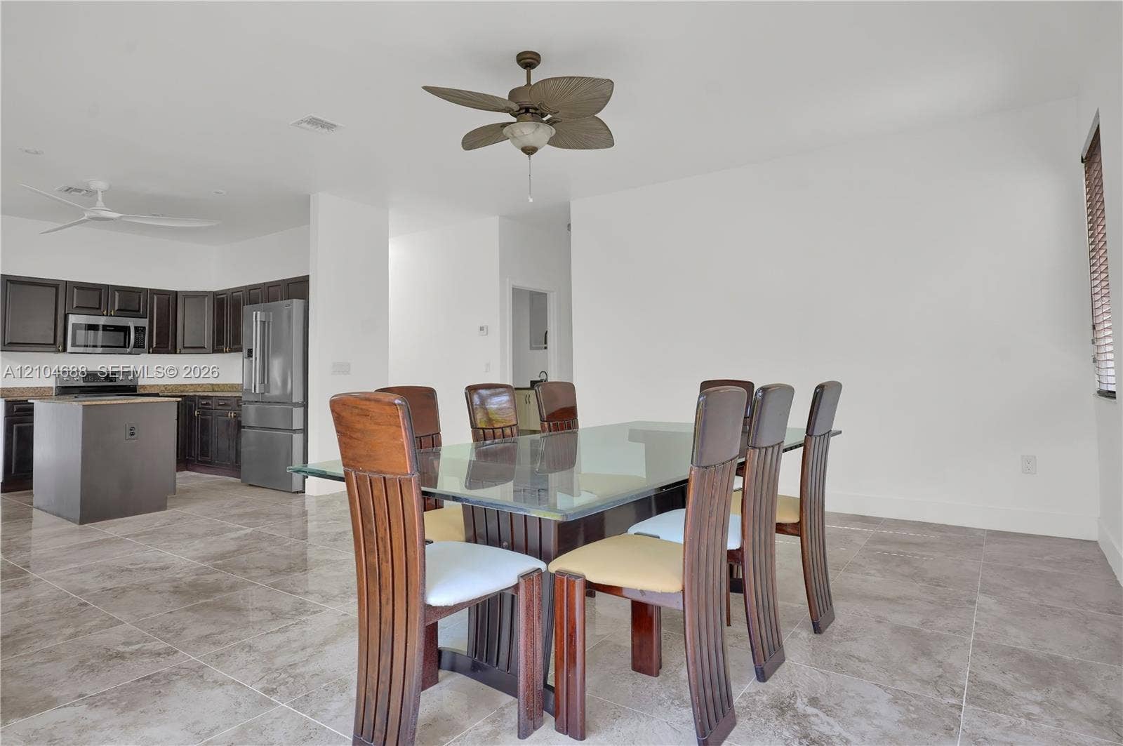 Open floor plan featuring large-format stone-style tile flooring, dark wood-finish cabinetry, a central kitchen island, and multi-blade ceiling fans