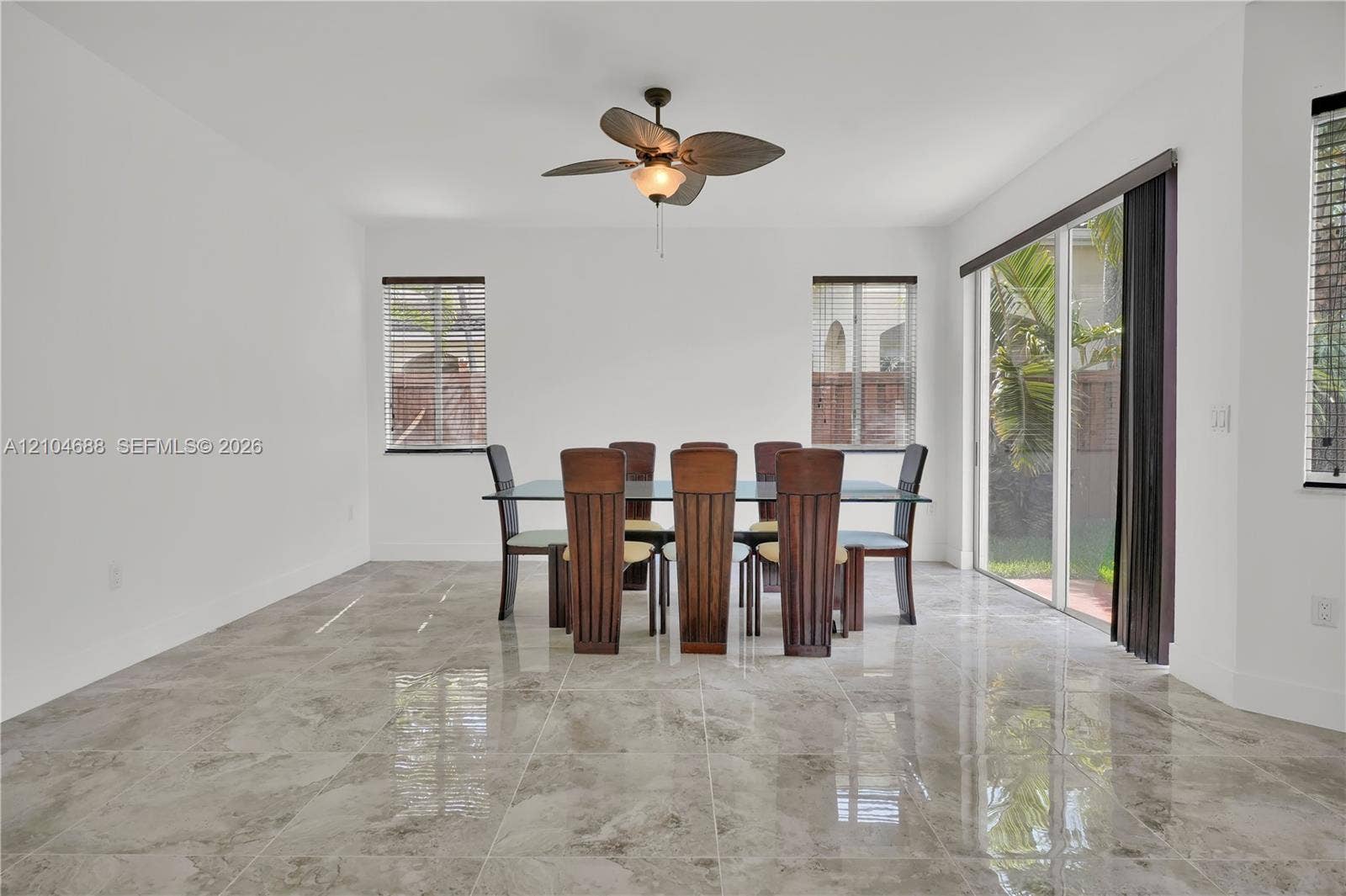 Large-format polished stone flooring, sliding glass patio doors, and a decorative ceiling fan with integrated lighting