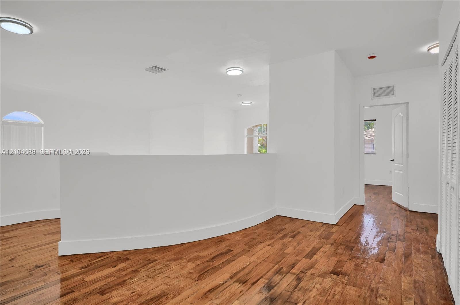 Open-plan space featuring wood-finish flooring, curved partition wall, arched windows, and louvered closet doors