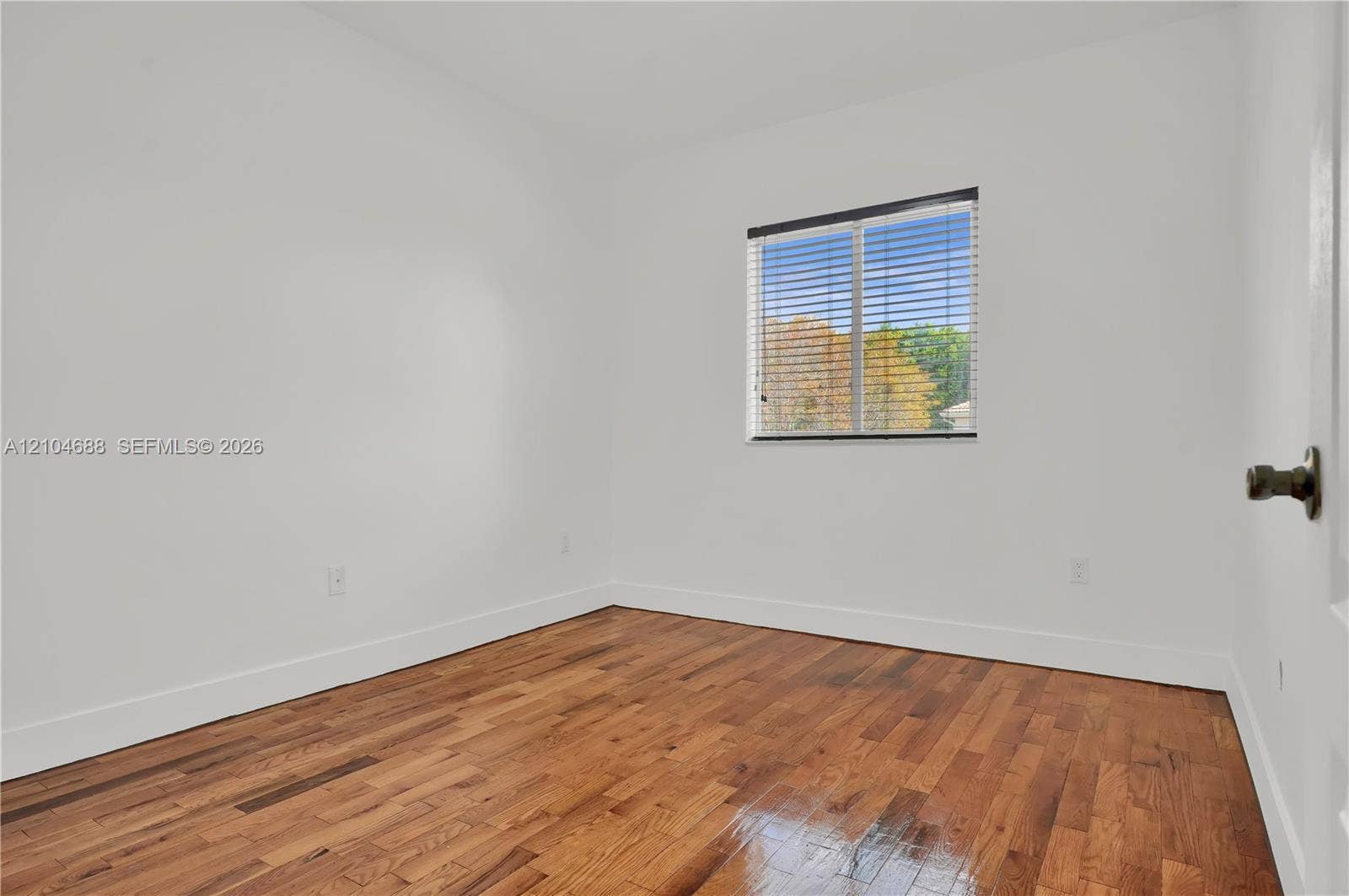 Interior space featuring wood-finish flooring, white walls, and a single window with horizontal blinds