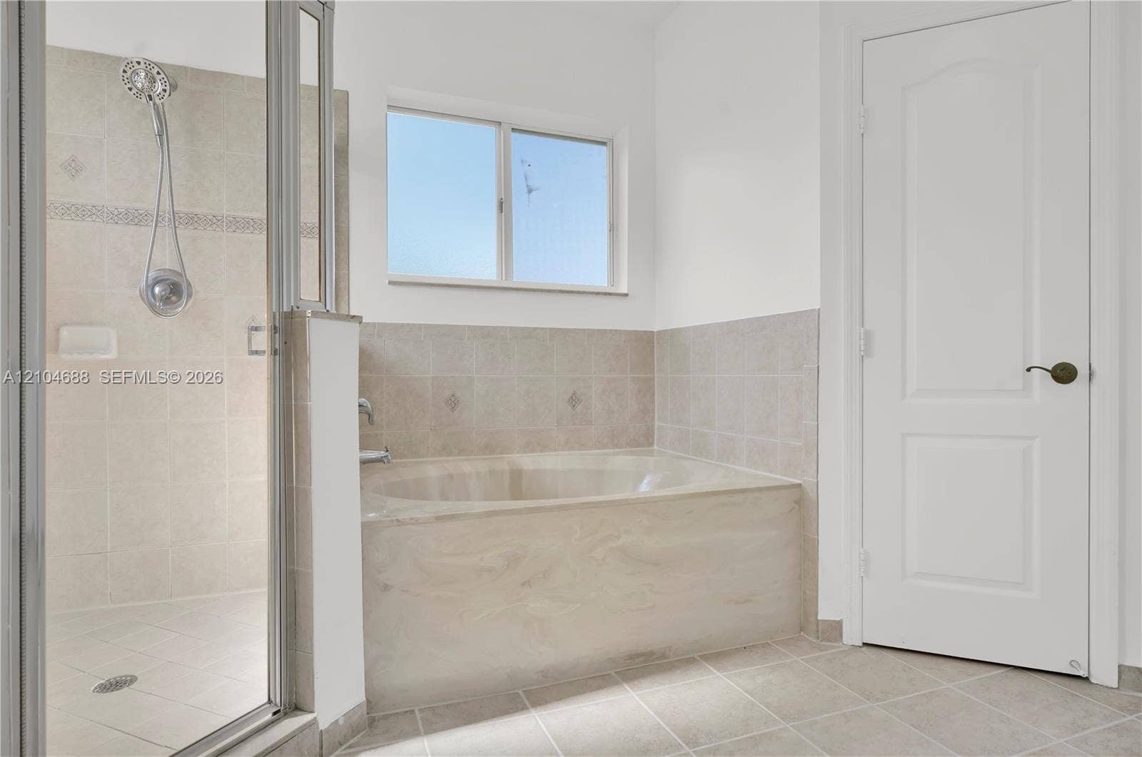 Soaking tub with tile surround, separate walk-in shower with glass enclosure, handheld shower fixture, and ceramic tile flooring