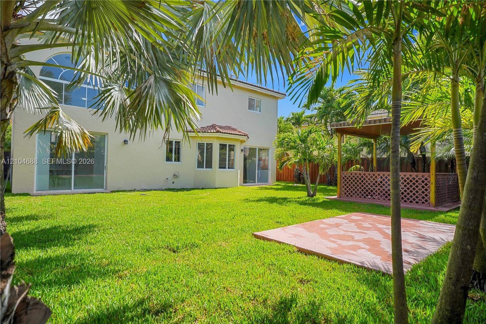 Rear exterior featuring a stucco facade, multiple sliding glass doors, a manicured lawn, a paved patio area, and a wooden gazebo