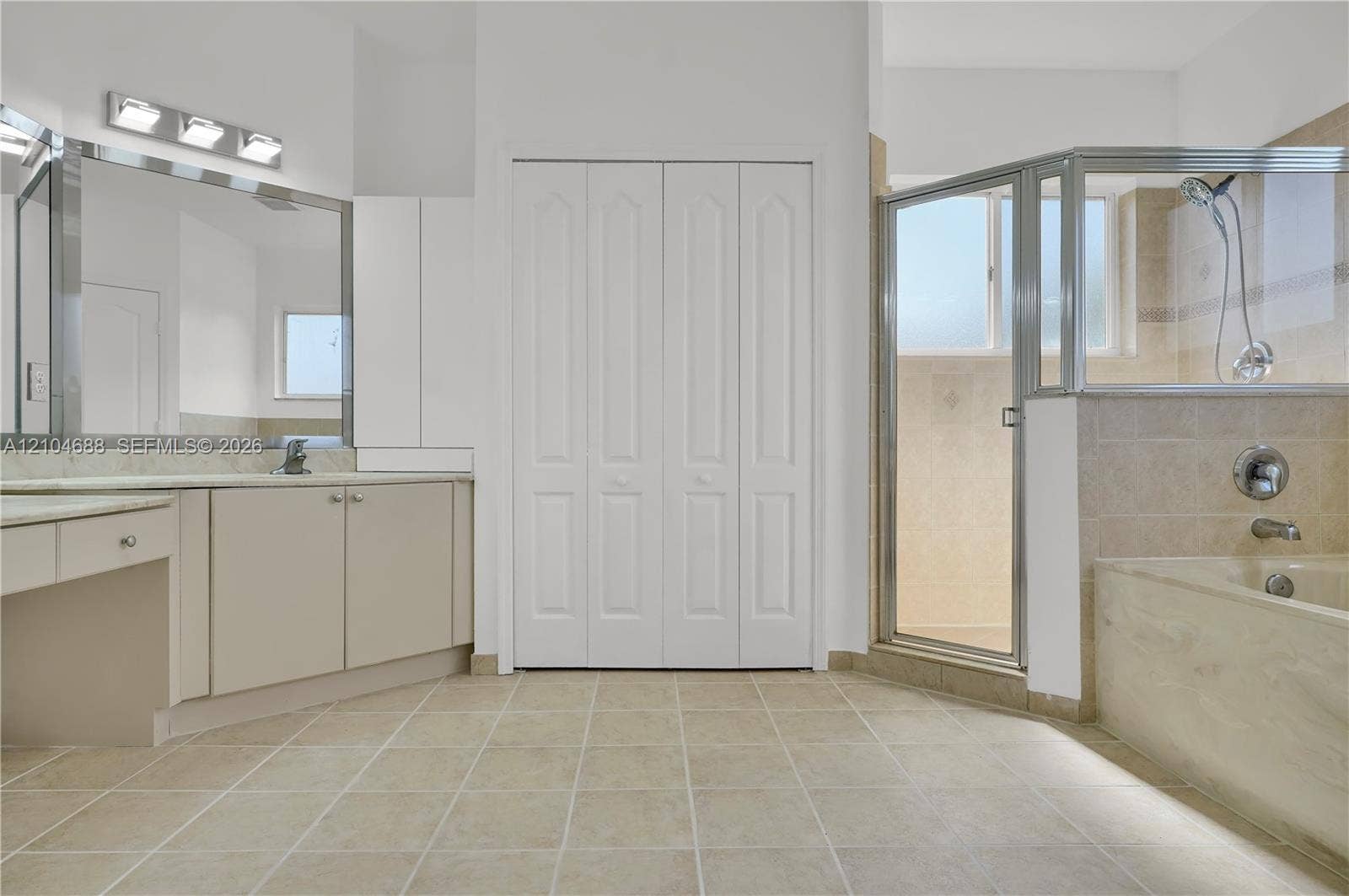 Bathroom featuring a vanity with a large mirror, a tiled soaking tub, a glass-enclosed shower, tile flooring, and floor-to-ceiling bi-fold closet doors