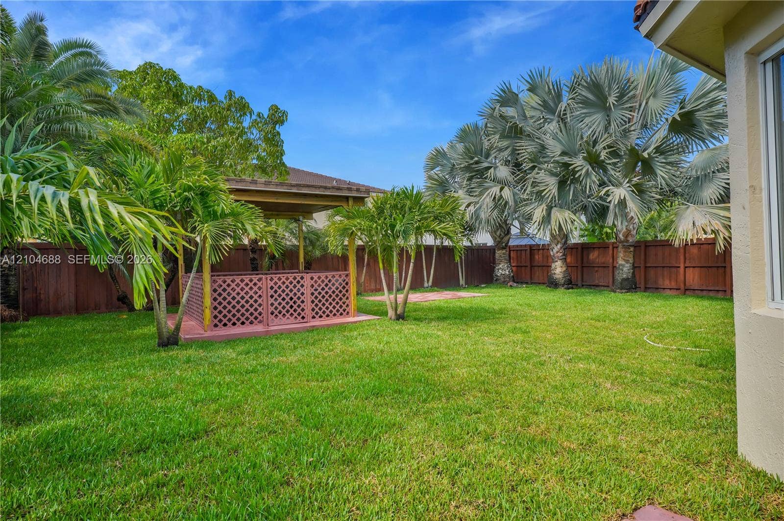 Private backyard featuring a manicured lawn, wooden lattice gazebo, full-perimeter wood fencing, and established palm trees