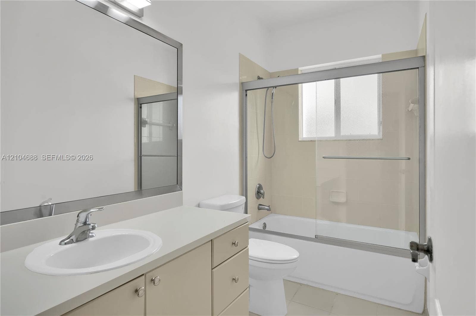 Bathroom featuring a solid-surface countertop with an integrated basin, large-format mirror with a metallic frame, vanity cabinet storage, and a bathtub with a sliding glass enclosure