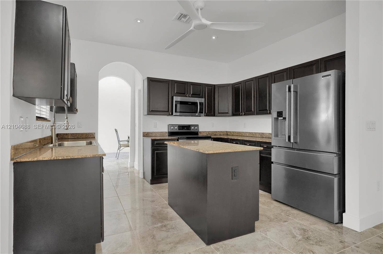 Kitchen featuring dark cabinetry, stone countertops, stainless steel appliances, a central island, and tile flooring