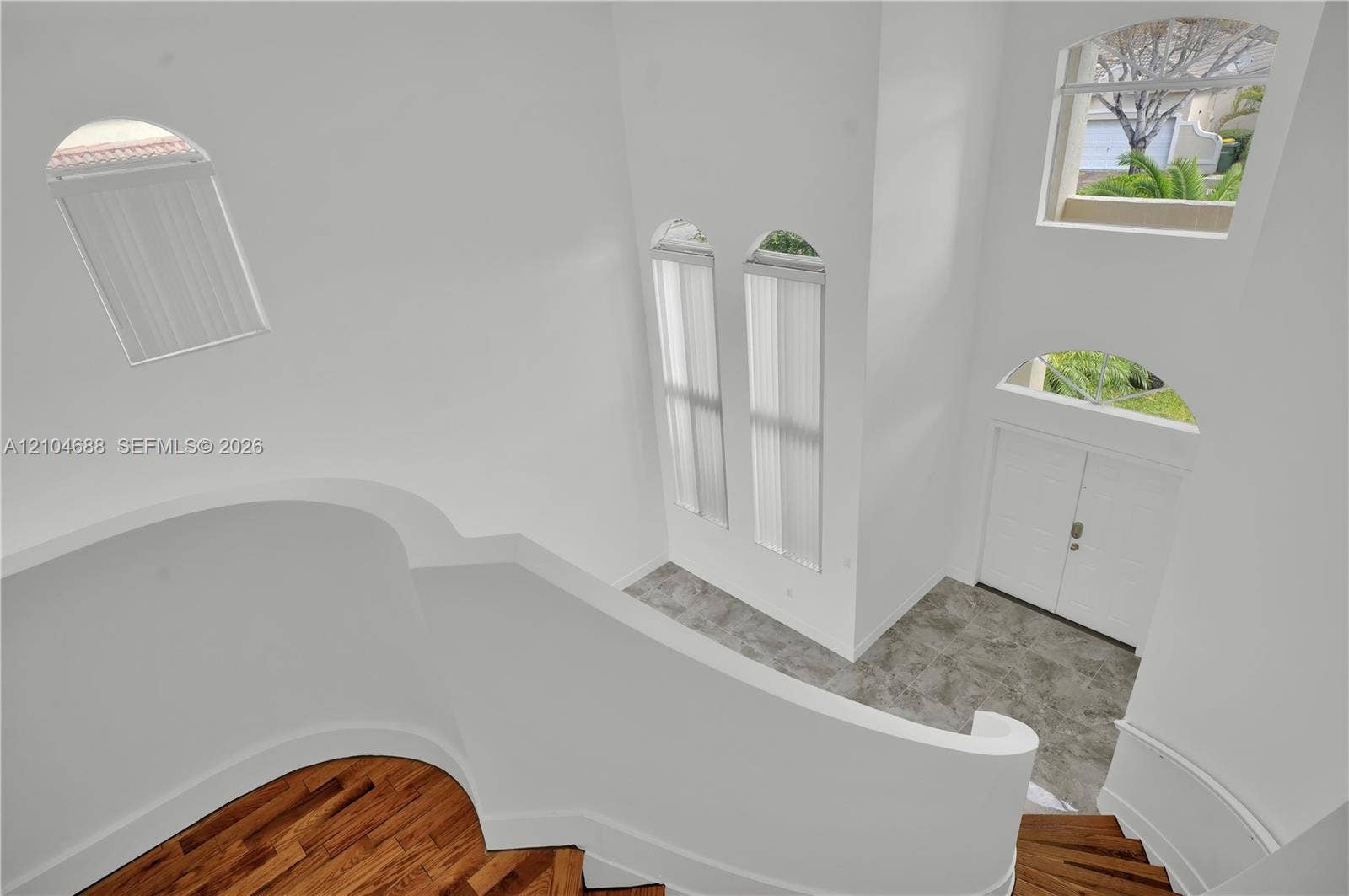 Foyer featuring a double-door entrance, stone-finish flooring, curved staircase with wood-finish treads, and multi-level arched windows