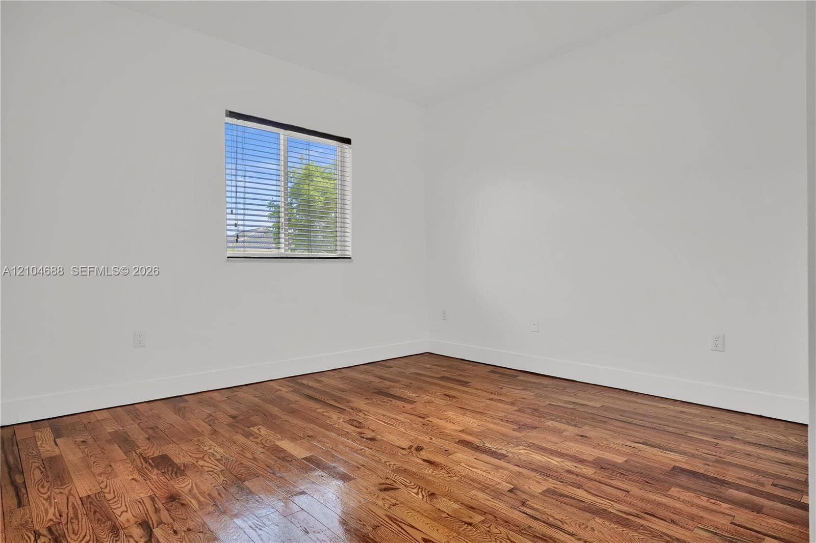 Interior space featuring wood-finish flooring, white walls, and a window with installed horizontal blinds