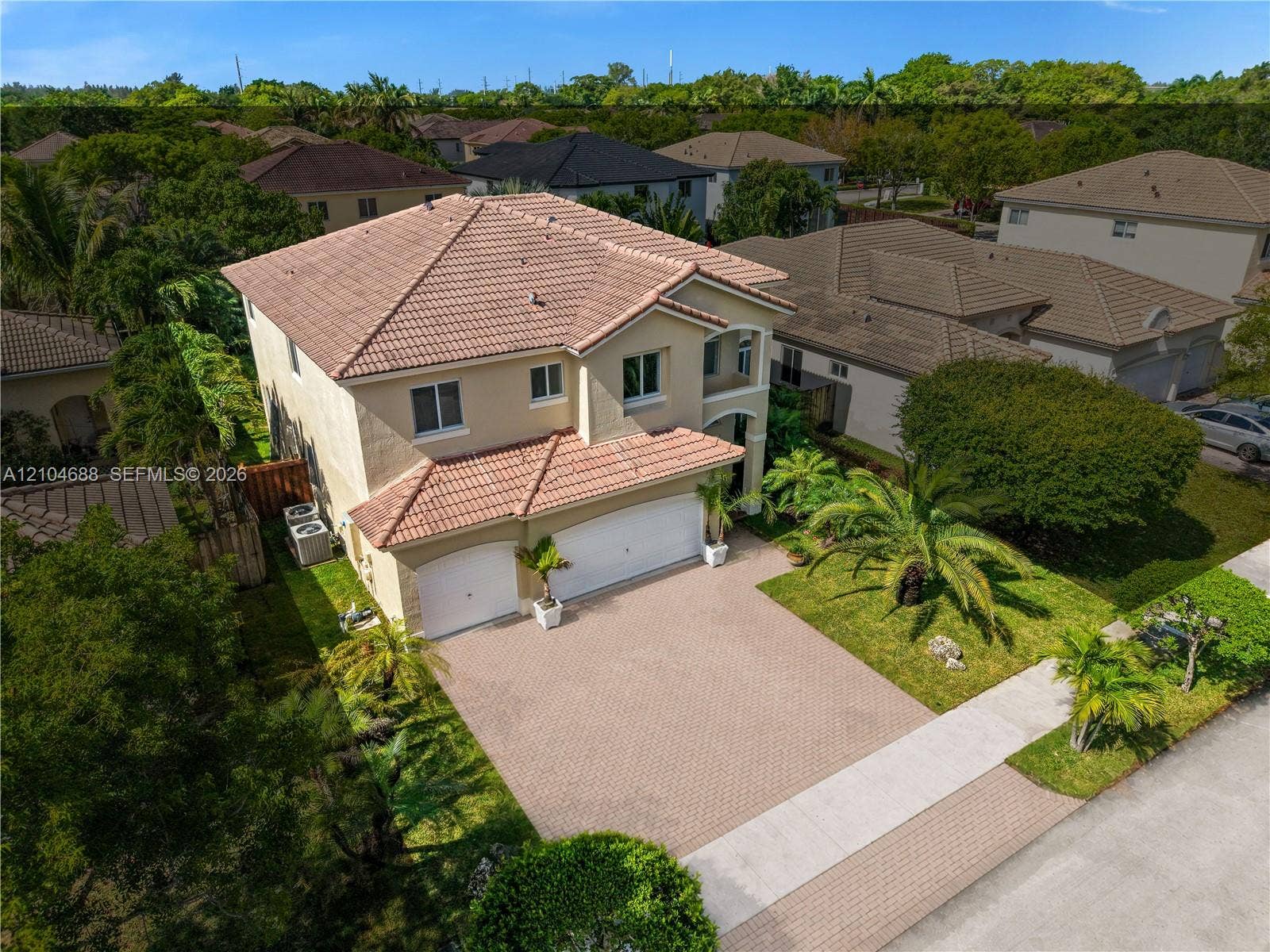 Two-story stucco exterior featuring a tile roof, brick-paver driveway, and a three-car garage