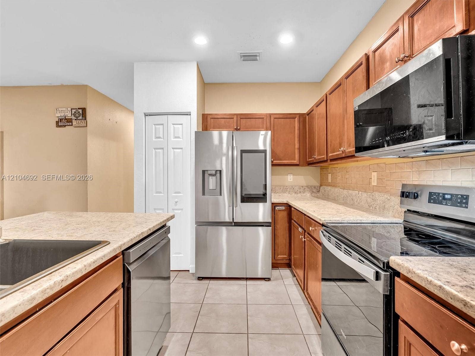 714 SE 37th Place, Homestead, FL 33033 Kitchen featuring warm-toned wood cabinetry, neutral countertops, tile flooring, and integrated stainless steel appliances