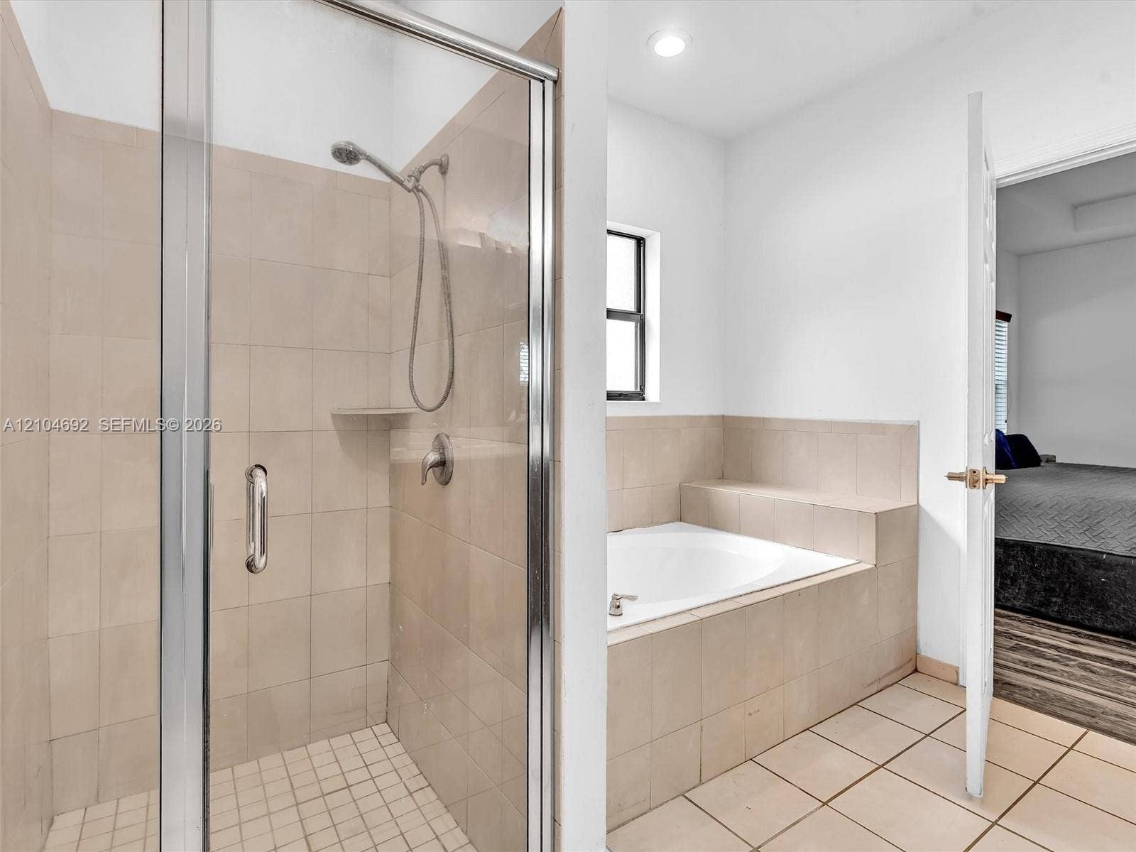 714 SE 37th Place, Homestead, FL 33033 Shower enclosure featuring a glass door, neutral-toned wall tiles, a built-in recessed shelf, and a detachable showerhead, paired with a built-in soaking tub surrounded by matching tile finish
