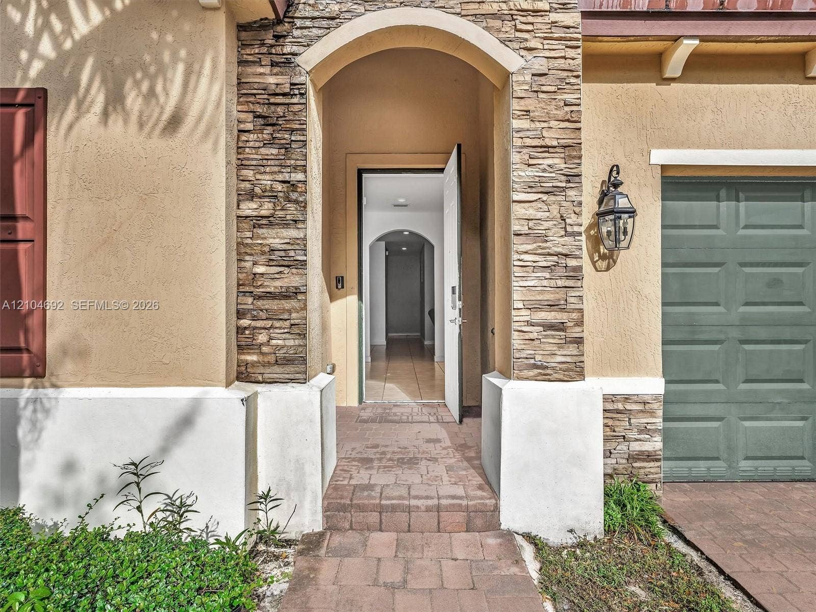 714 SE 37th Place, Homestead, FL 33033 Stucco exterior featuring stacked stone accents, an arched entryway, paver walkway, and a carriage-style garage door with an attached wall-mounted lantern