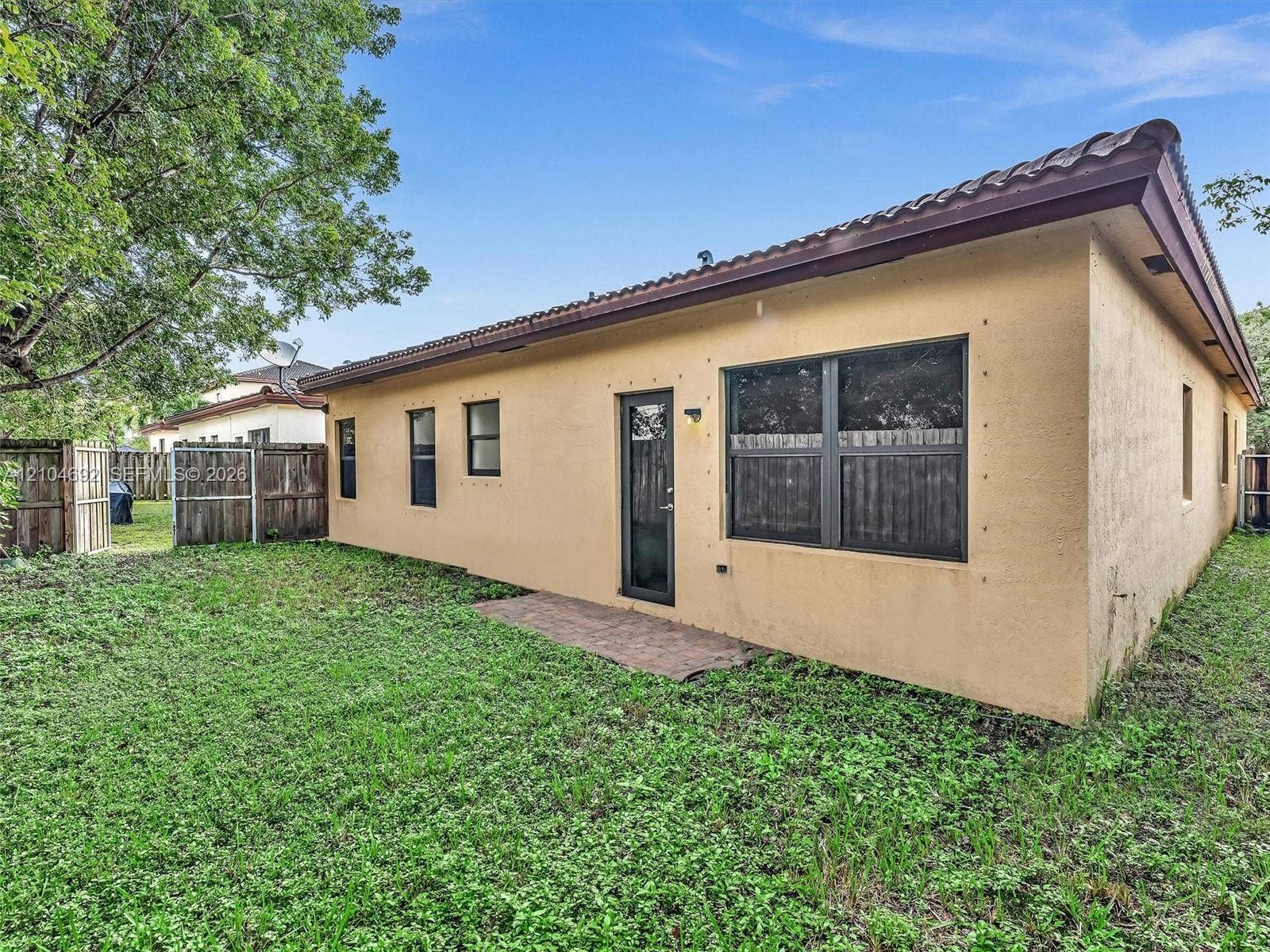 714 SE 37th Place, Homestead, FL 33033 Stucco exterior featuring a tile roof, paved rear patio, single-light glass door, and wooden perimeter fencing