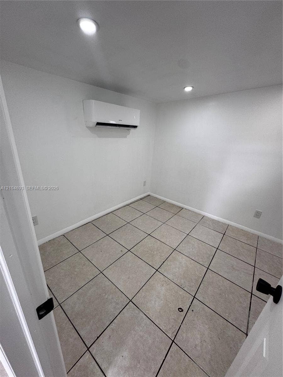 Recessed ceiling lighting, wall-mounted air conditioning unit, light-toned tile flooring, white walls, and white trim