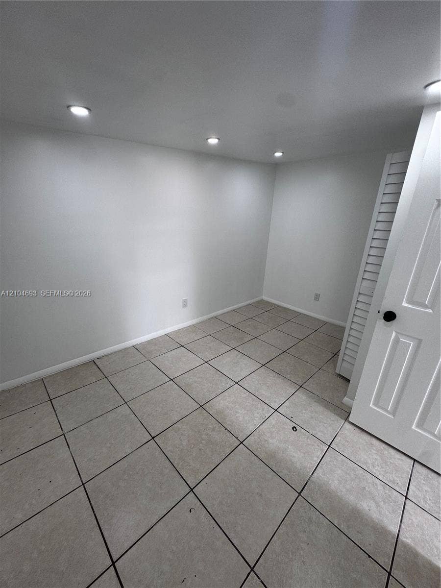 Recessed ceiling lighting, light gray wall finishes, square tile flooring, and a white paneled door