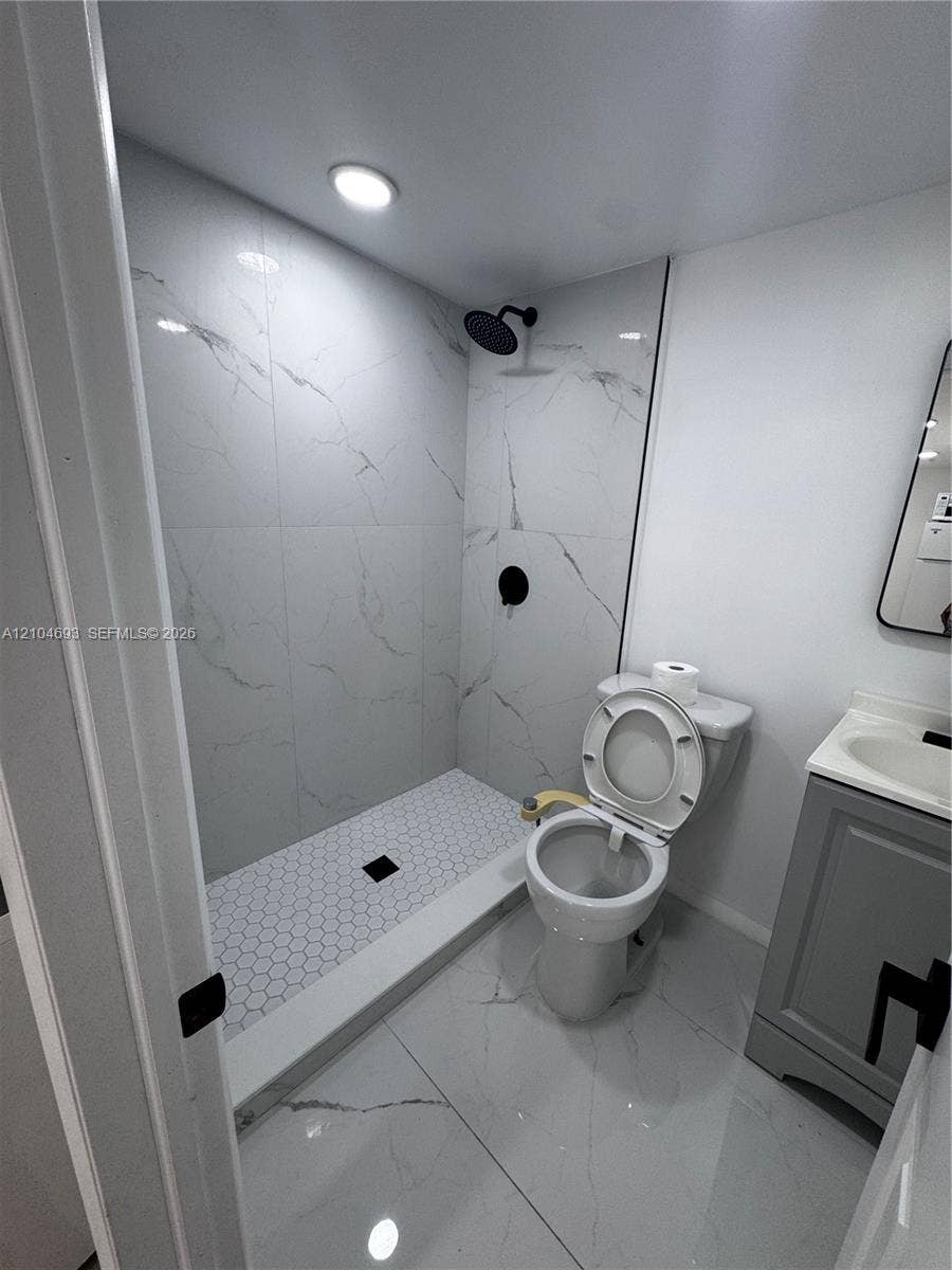 Walk-in shower with hexagonal tile floor, wall-mounted showerhead, and black fixtures