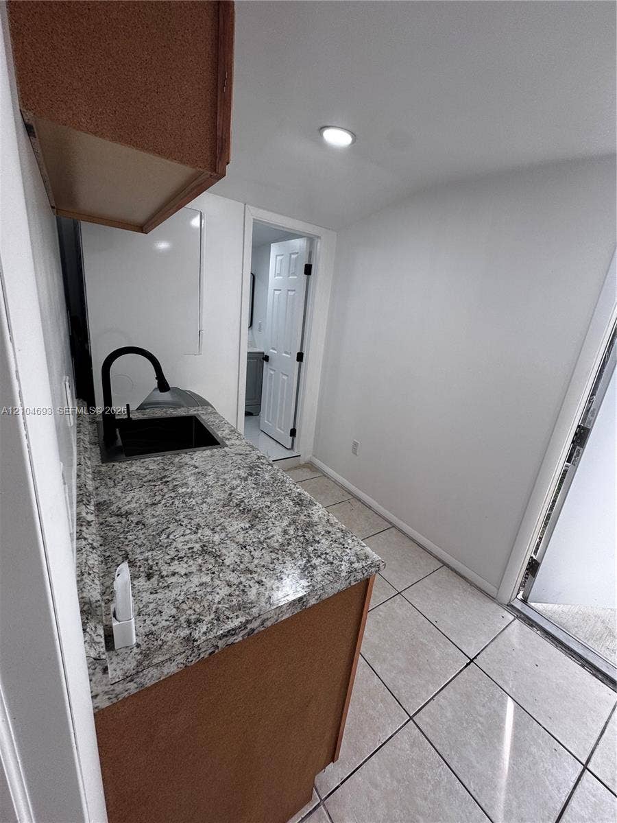 Recessed lighting, wood-finish cabinetry, granite-style countertop, undermount sink with a matte black faucet, and tiled flooring