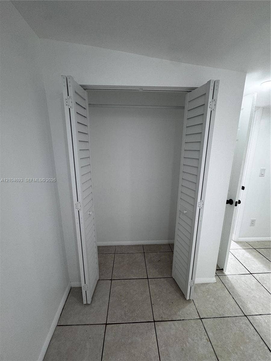 Closet with bi-fold louvered doors, interior hanging rod, and tile flooring