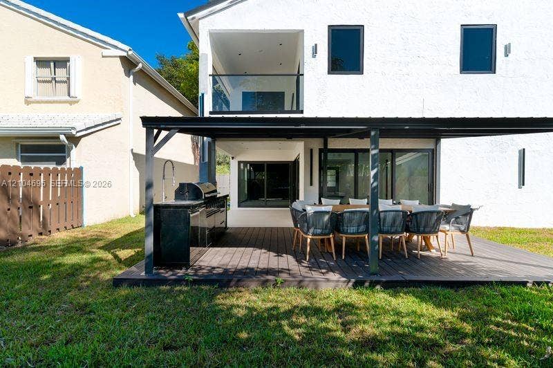 9963 NW 2nd Court, Plantation, FL 33324 Stucco exterior featuring a covered patio with a dark wood-finish deck, integrated outdoor kitchen, and a glass-railed upper-level balcony