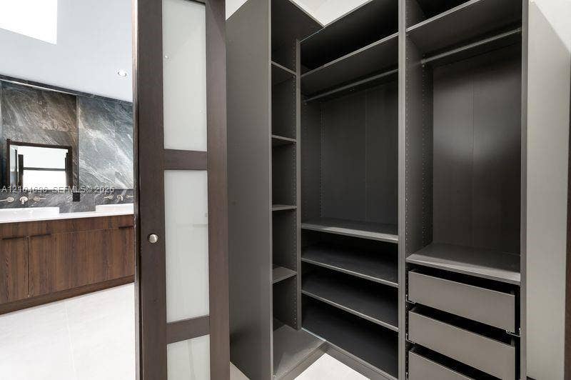 9963 NW 2nd Court, Plantation, FL 33324 Custom built-in dark finish closet shelving with integrated drawers and hanging rods, featuring a sliding door with frosted glass panels, wood-finish cabinetry, and stone-surround wall tiling